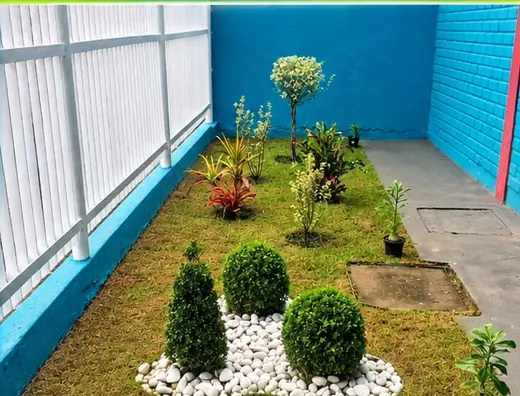 Quintal com grama aparada, canteiro de pedras brancas e arbustos podados